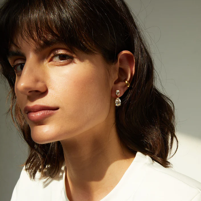 Pear-cut drop earrings and a gold huggie worn on an ear